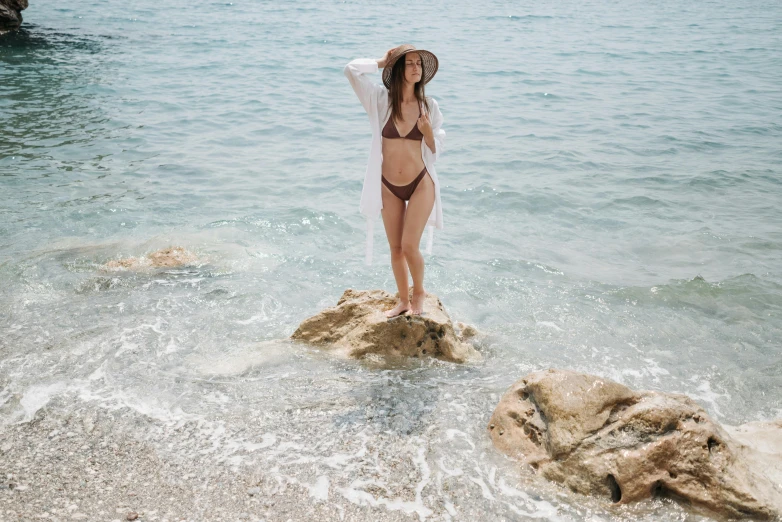a woman in a bikini standing on rocks looking out at the water