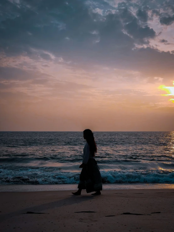 a woman walking on the beach at sunset