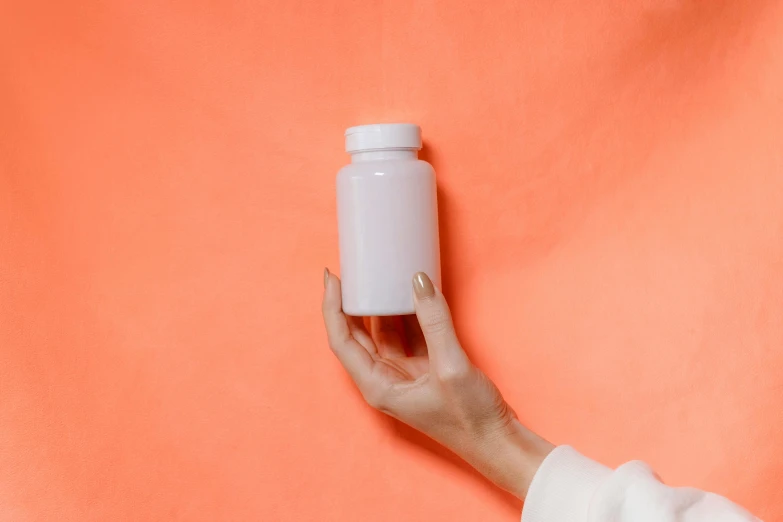 a hand holds a white empty bottle on an orange background