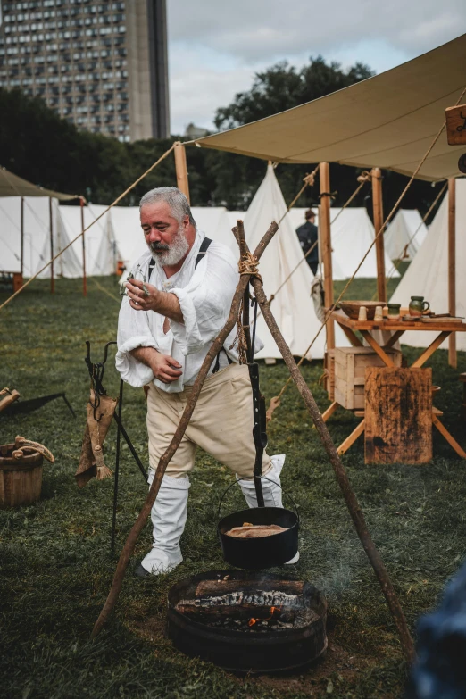 an older man holding a stick next to an open fire