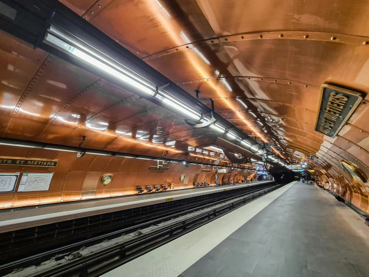 a subway platform with gold tile walls and a steel and white escalator