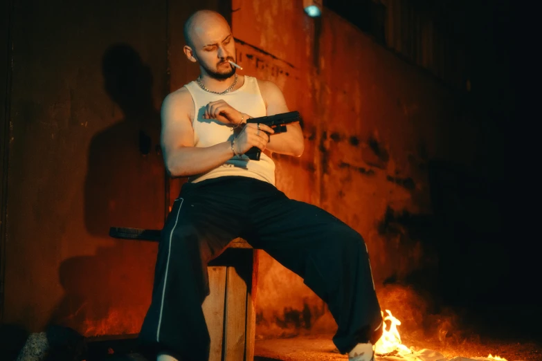 man with cigarette, white shirt and dark pants, sitting on bench next to fire