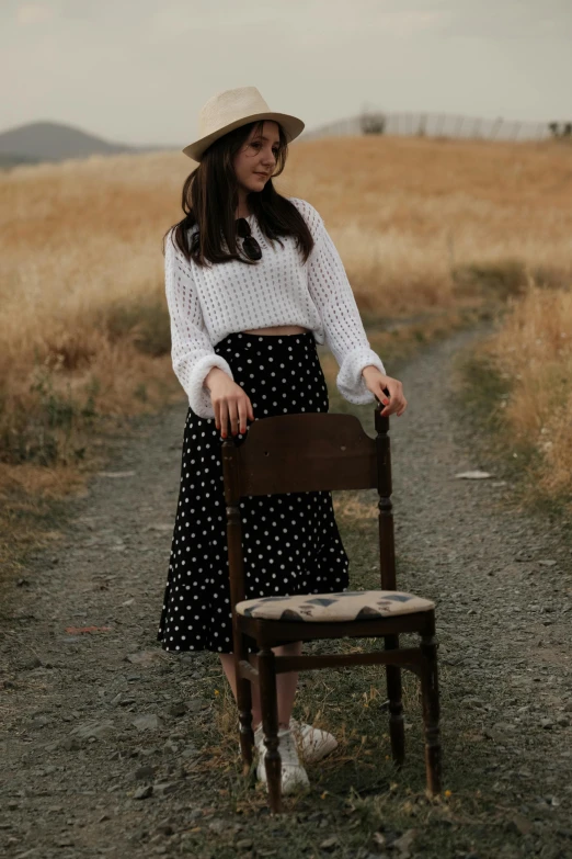 a woman standing near a wooden chair in a field