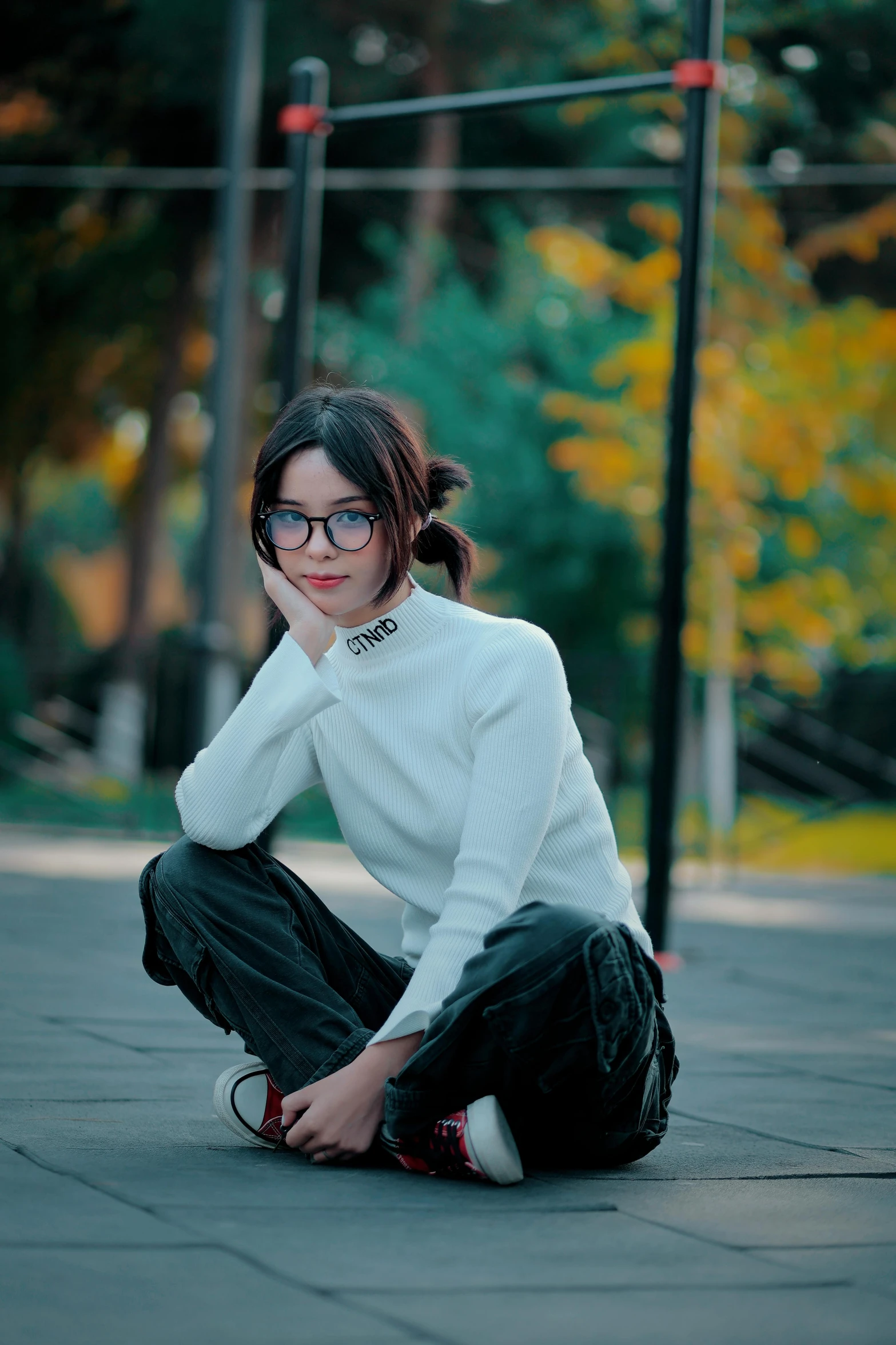 woman with black glasses, white shirt and black pants crouching on the street