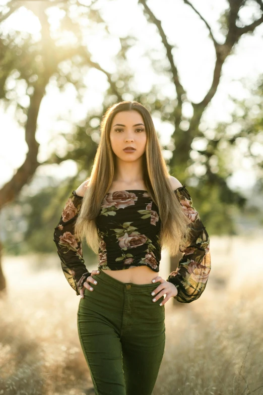 a beautiful woman wearing green pants poses in the sunlight