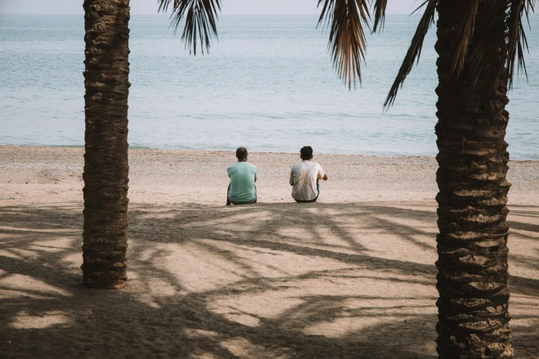 two people sitting on top of the beach under palm trees