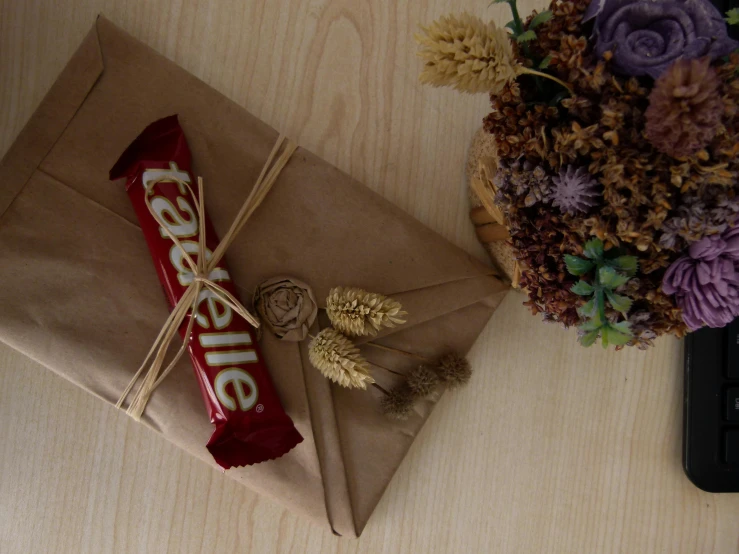 chocolate bar wrapped with candy sits on top of a gift bag next to a bouquet of dried flowers