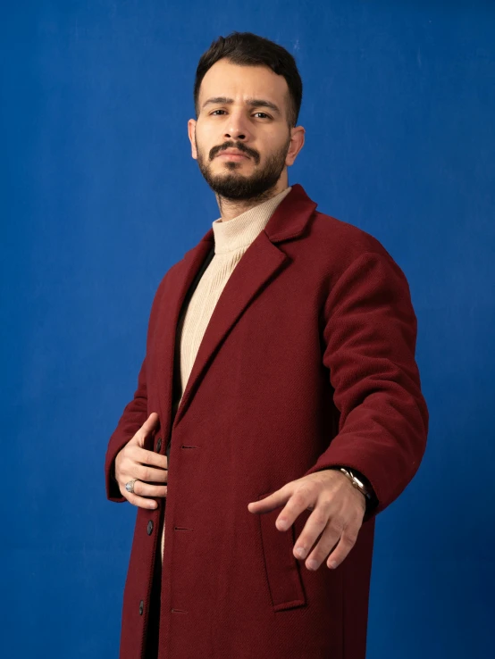 man standing and gesturing on blue background wearing a burgundy coat