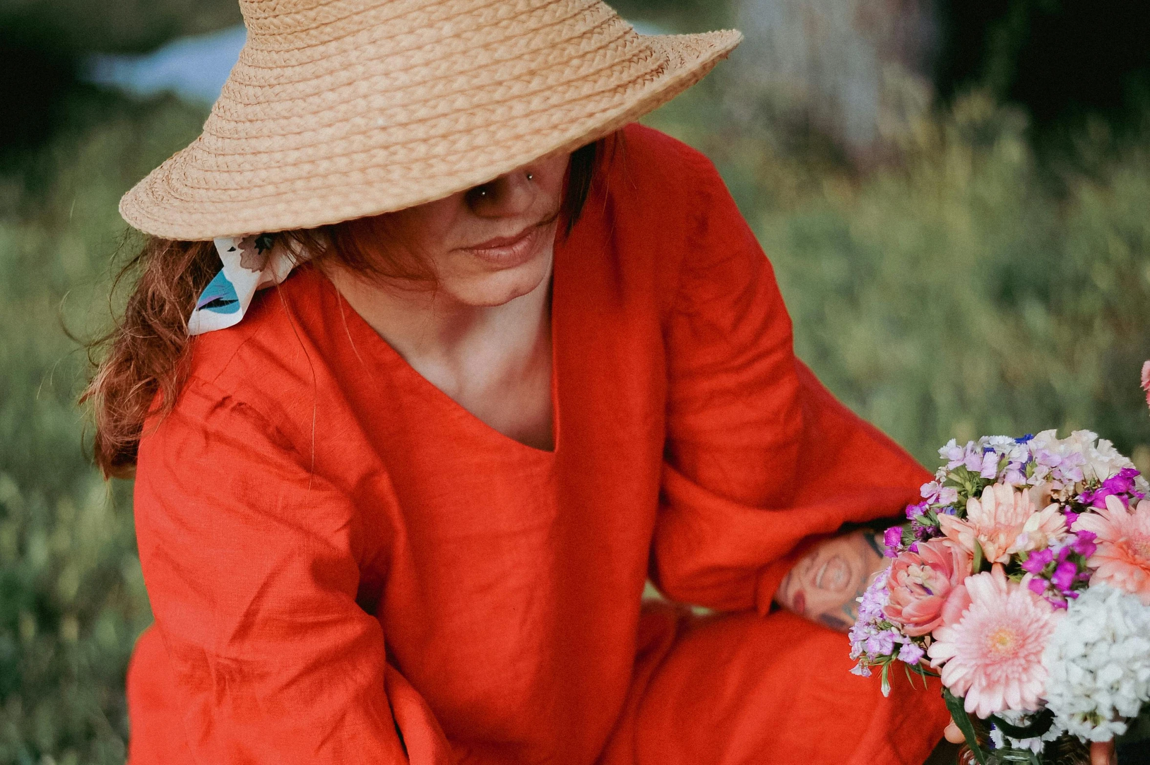 a woman with red outfit and straw hat sitting down holding flowers