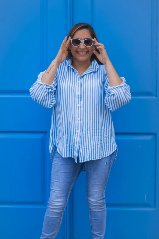 a woman in a blue and white shirt and jeans leaning on a blue garage door