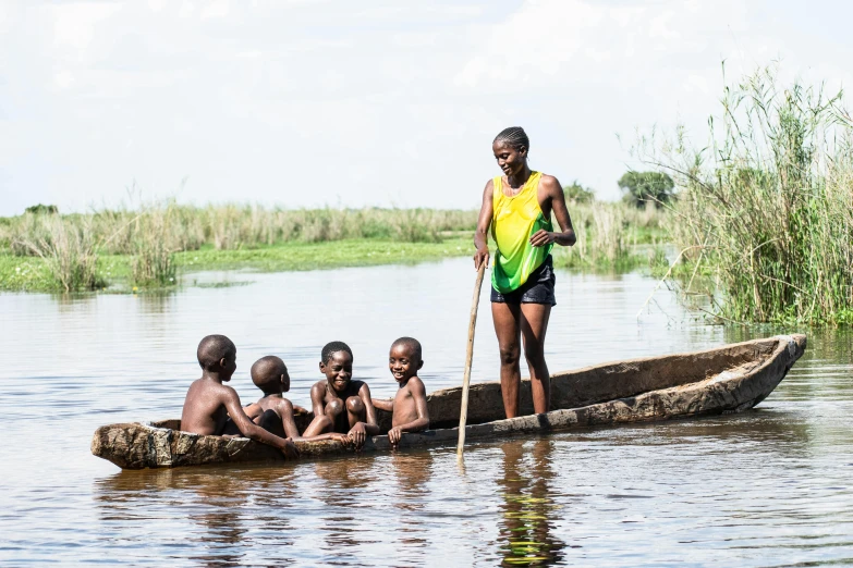 an older man stands in a row boat with seven children