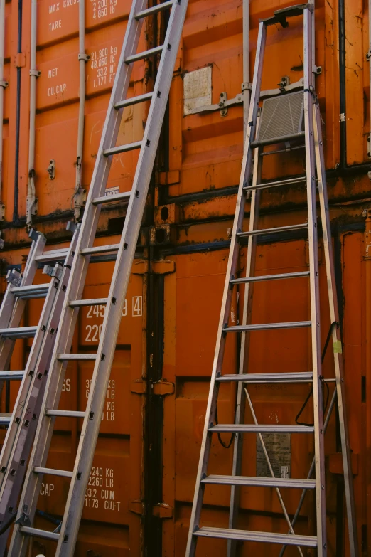 several ladders leaning against an orange wall with multiple metal words on it