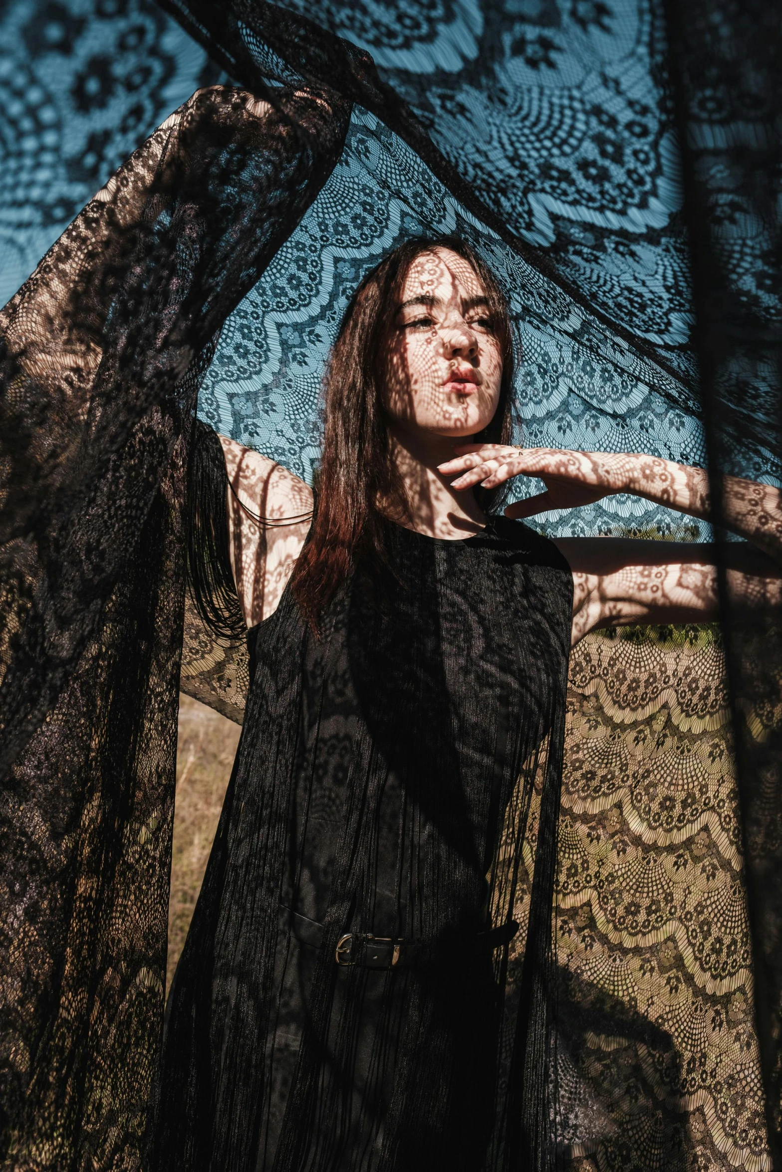 a woman posing beneath a black umbrella with her hands behind her back