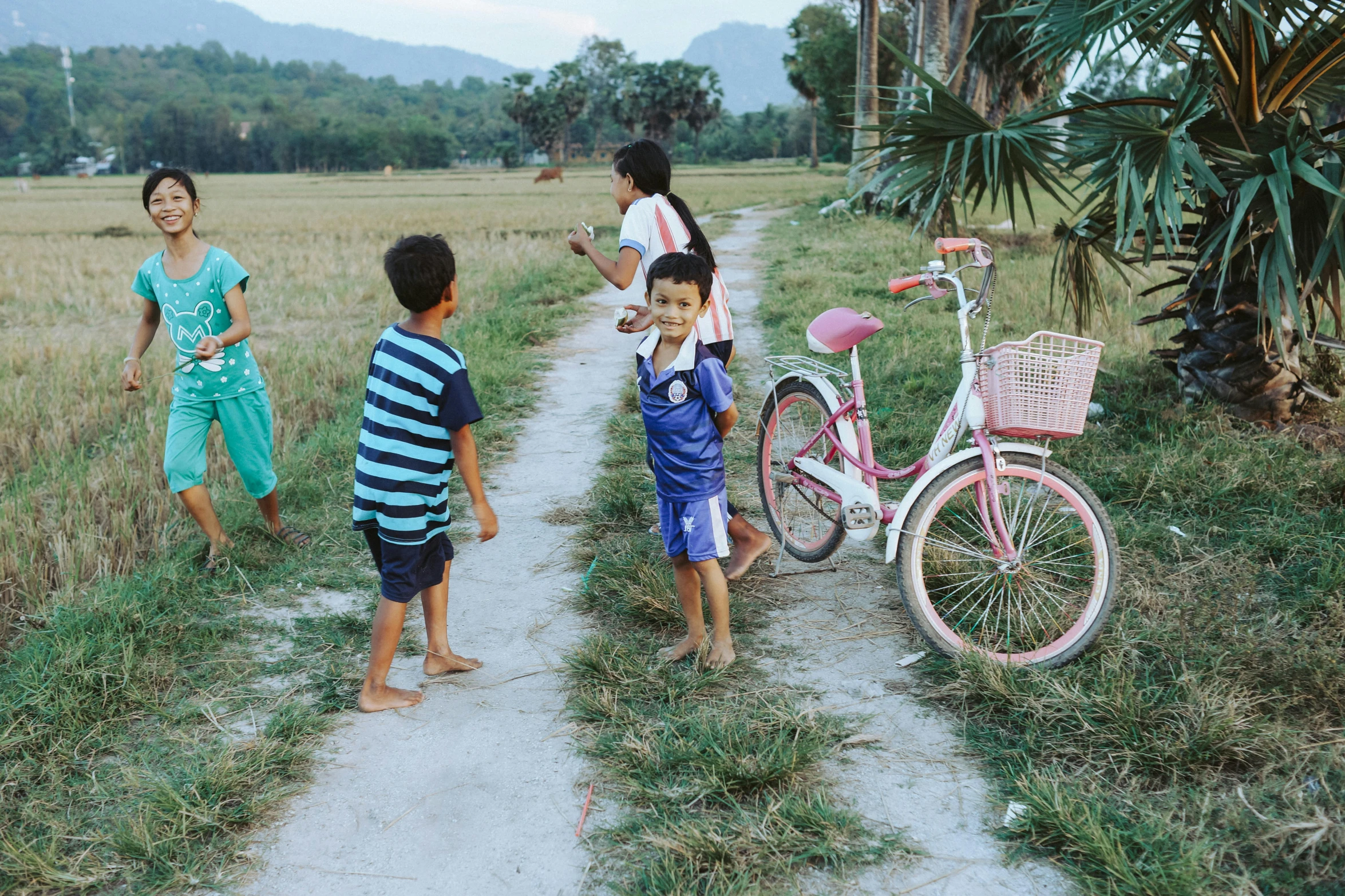 children are playing with their bikes on the side of a dirt road