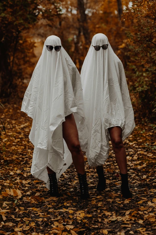 two ghost like women in white covers walk through a wooded area