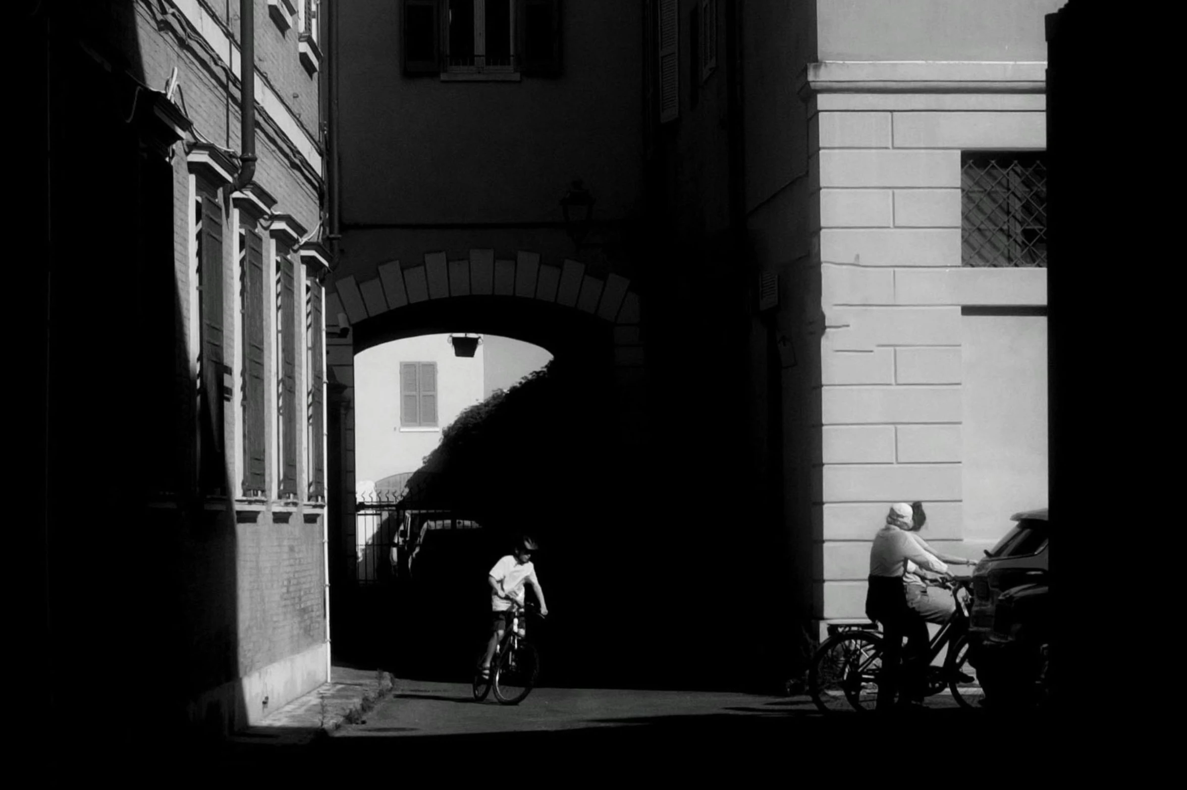 an alley between buildings with men standing and riding bikes in the street