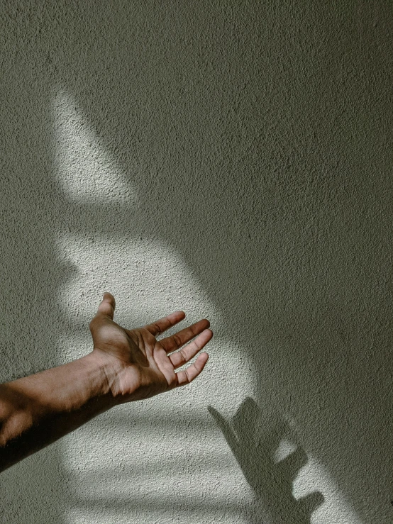 a hand with their arm outstretched in front of the shadow of a wall