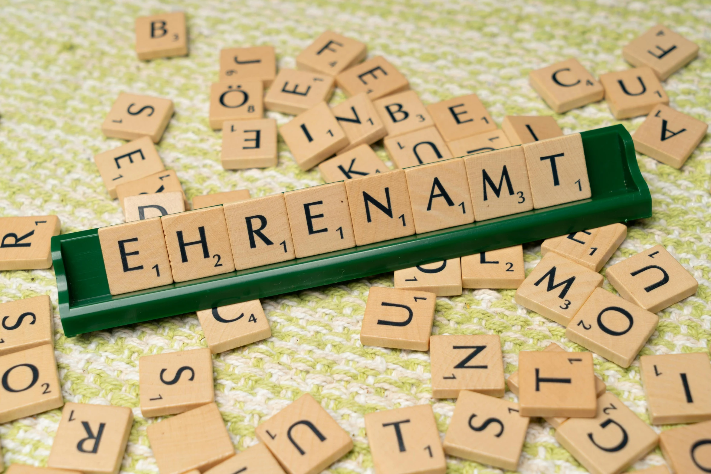 scrabble tiles with letters and a small block spell out the word ehernamt