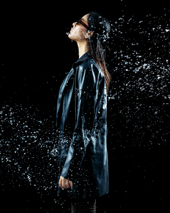 a woman stands in a black raincoat and drops of water on her face