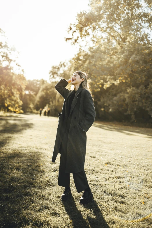 a woman with long hair in a long coat is standing on some grass