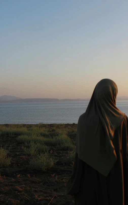 a person standing by the ocean with a cape on their head