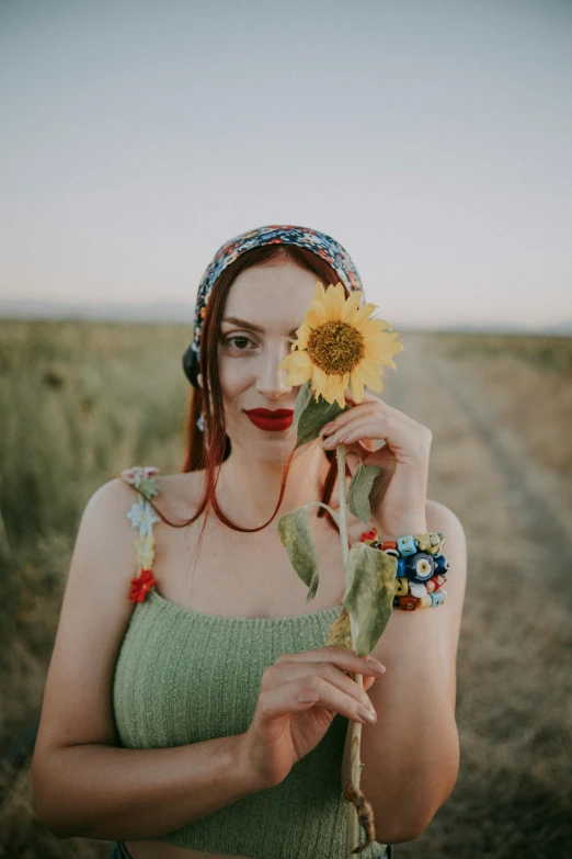 a woman holding a sunflower with her face near her