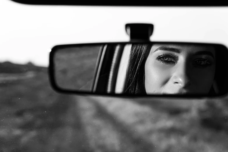 woman with hair in a black and white po taking her own picture in the rear view mirror