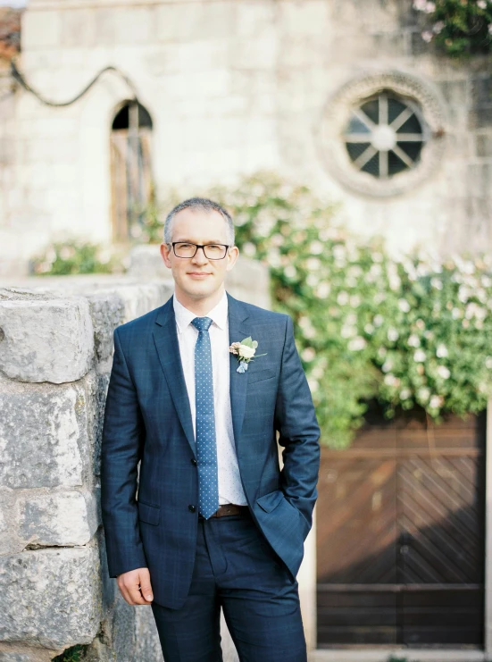 a man standing by a wall and wearing a suit