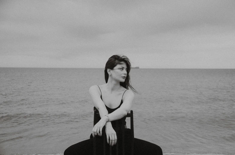 black and white pograph of woman sitting on beach next to water