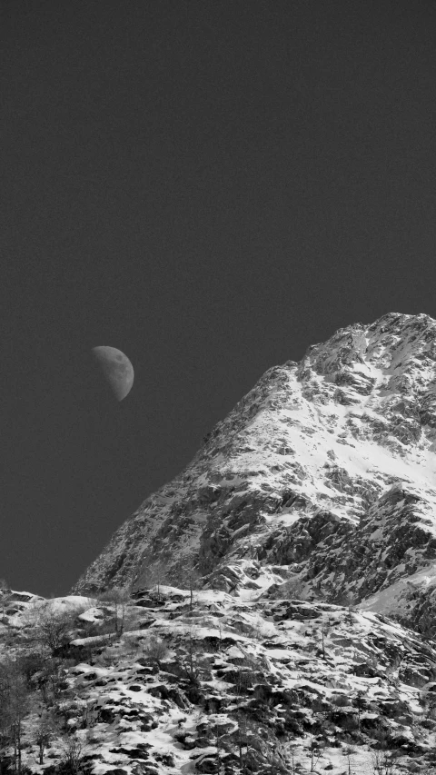 a half moon over a snowy mountain in black and white