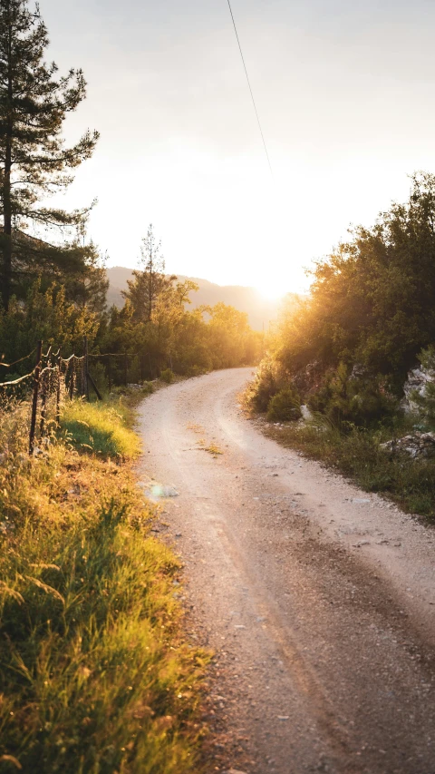 a dirt road next to a fence at the sunset