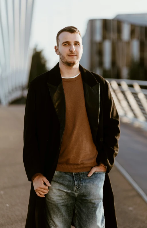 a man in a brown sweater, jeans and black coat