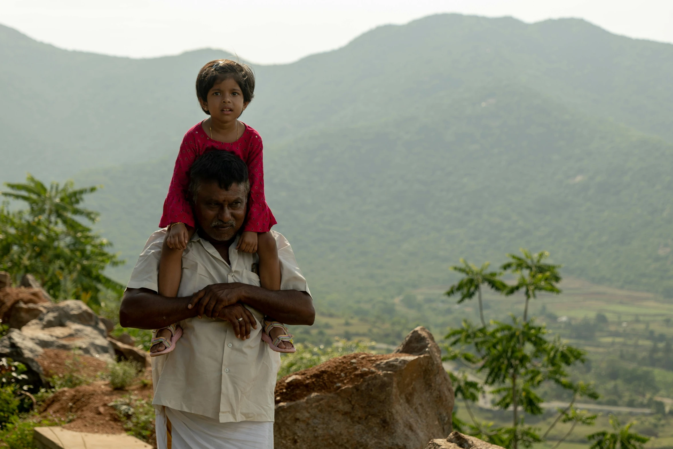 a man carrying a  on his shoulders with mountains and hills behind