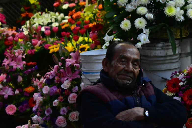 an elderly man standing next to bunches of flowers