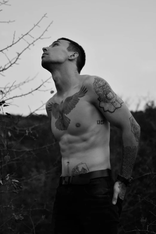 a black and white image of a man with tattoos looking upward