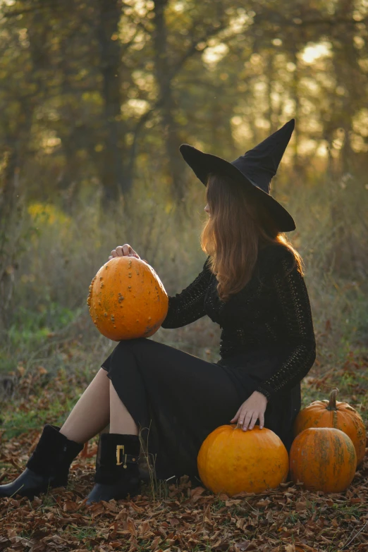 a woman sitting on a field with two pumpkins