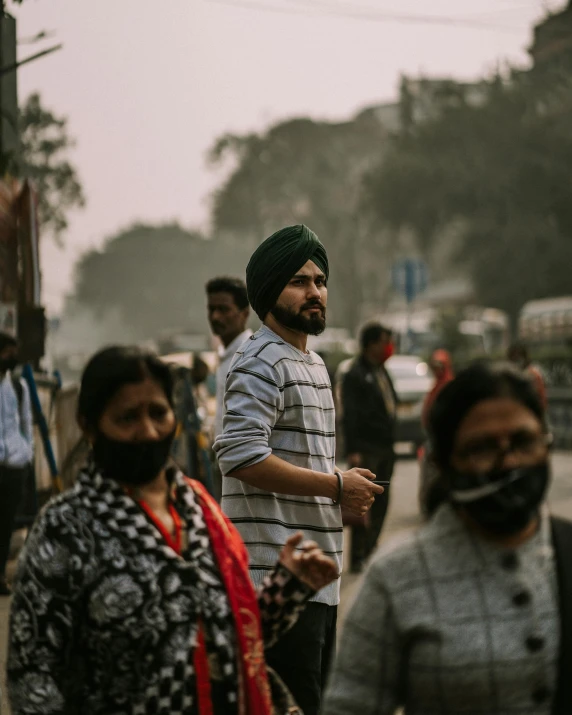 several people are standing near a sidewalk, one man wearing a green turban