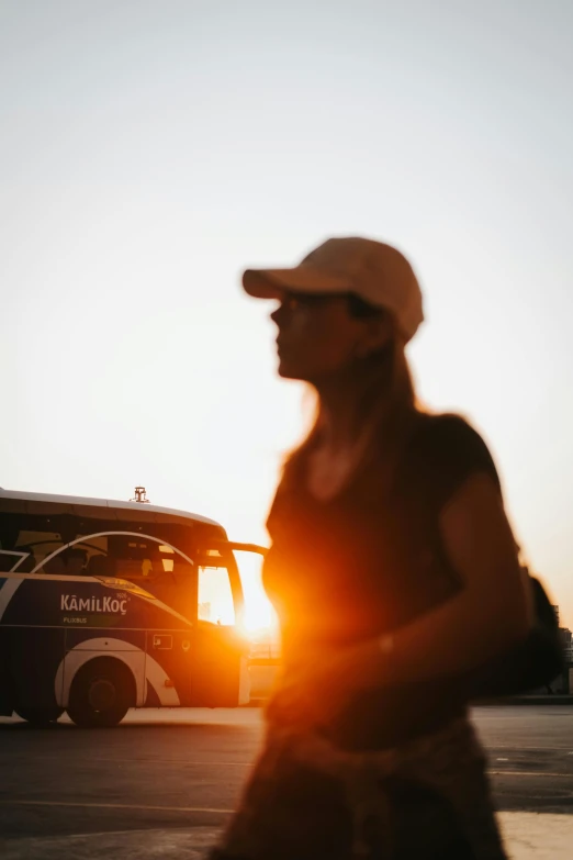 a woman in black shirt and hat walking next to a bus