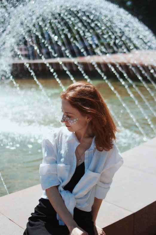 a woman with red hair is sitting on a ledge near a fountain