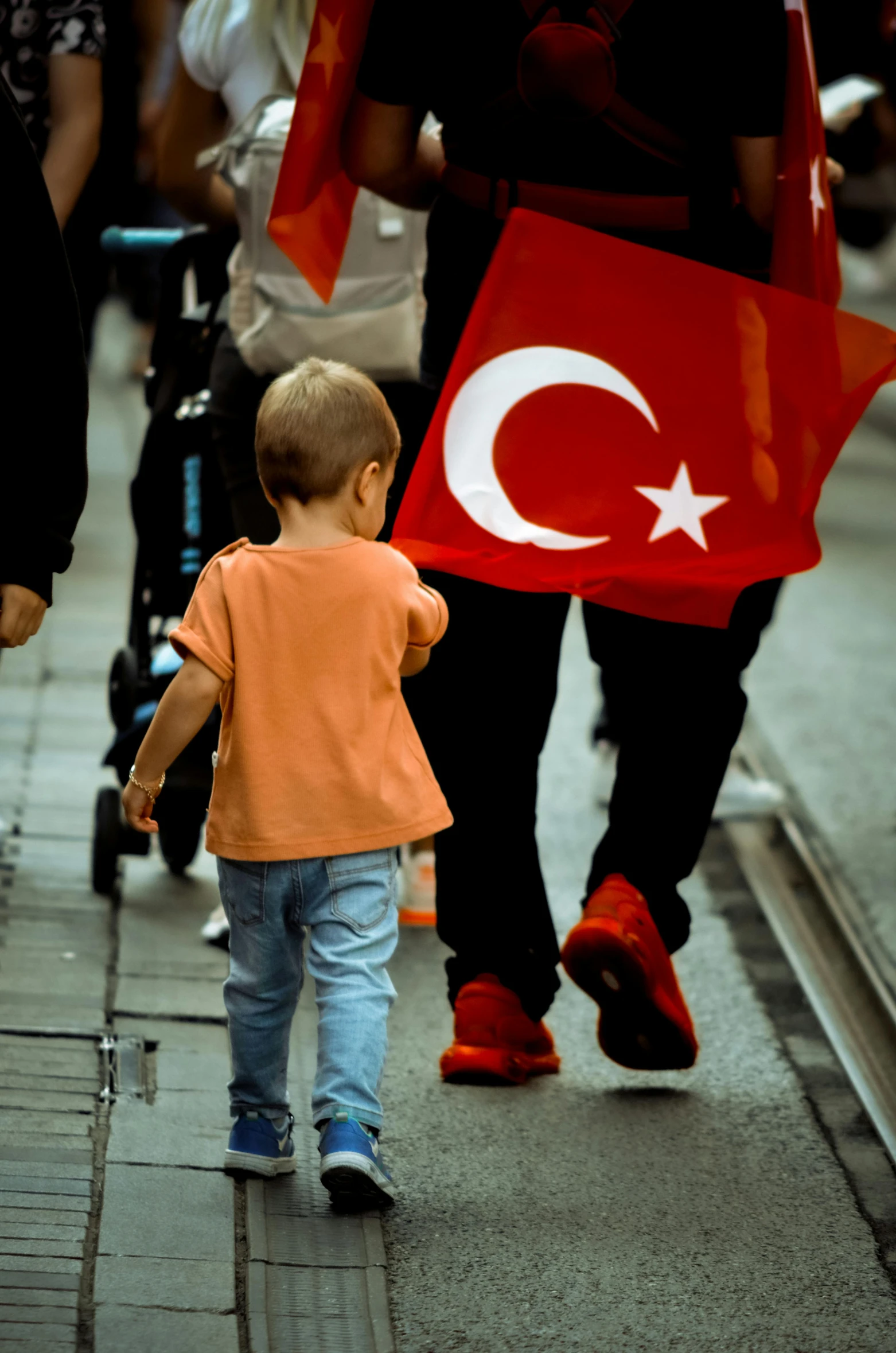 a small child walking down the sidewalk with some people