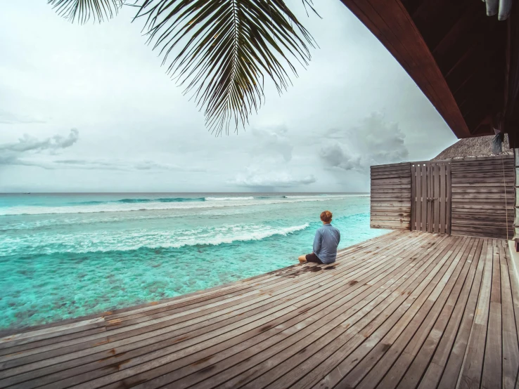 the man is sitting on a pier looking at a wave