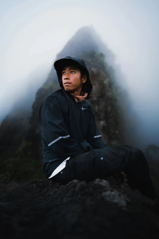 a boy in black jacket and cap sitting on rock