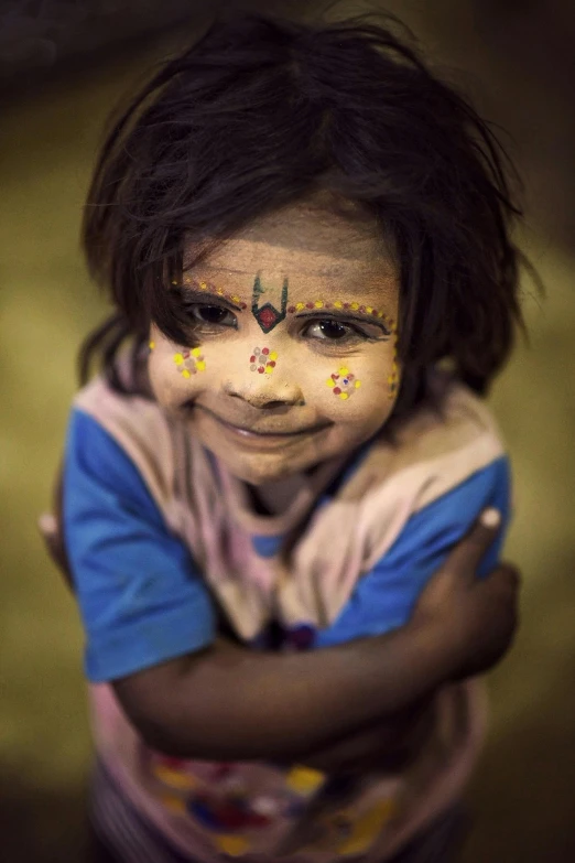 a child painted like a god wearing a blue t - shirt with face paint