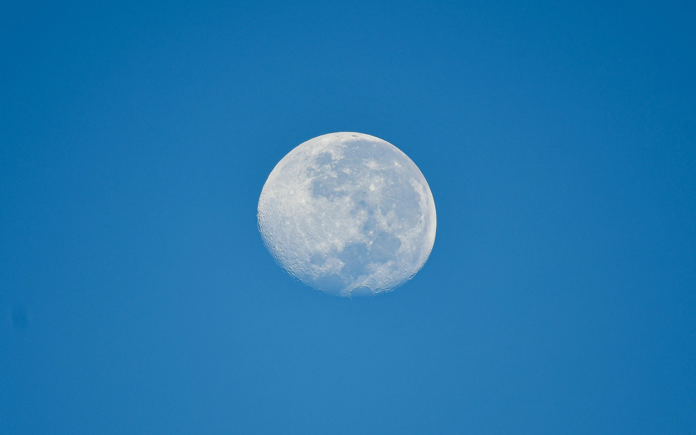 an airplane flies across the blue sky past a full moon