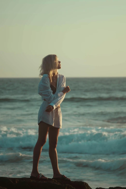 a woman stands on the rocks next to the ocean