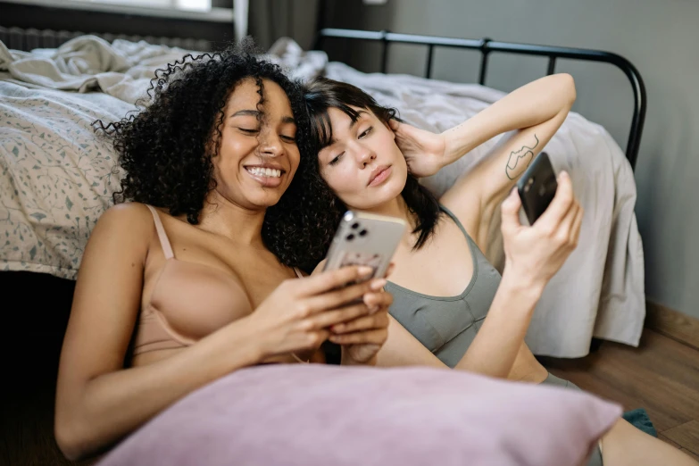 two girls on the bed while looking at a cellphone