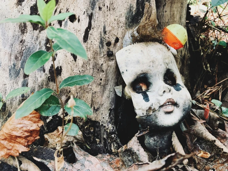 a doll with skull like hair and orange eyes stands against a tree