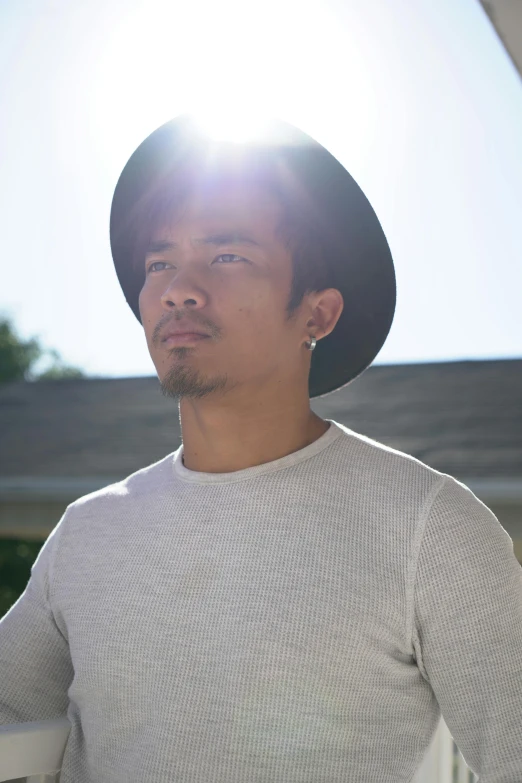 an asian man wearing a hat stands in the sun