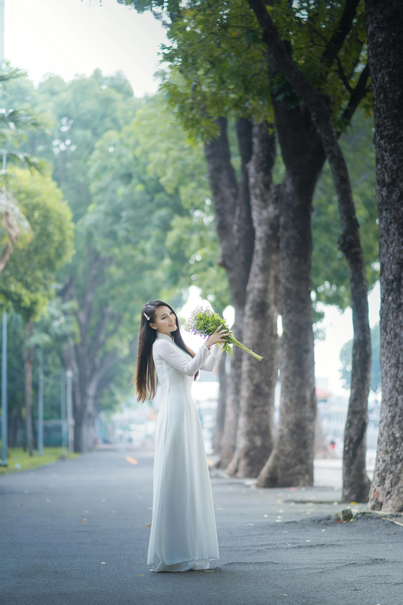 the young woman is standing in front of the trees and holding flowers