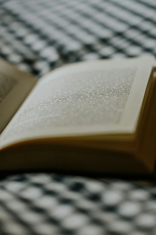 an open book laying on a bed next to a plaid cloth